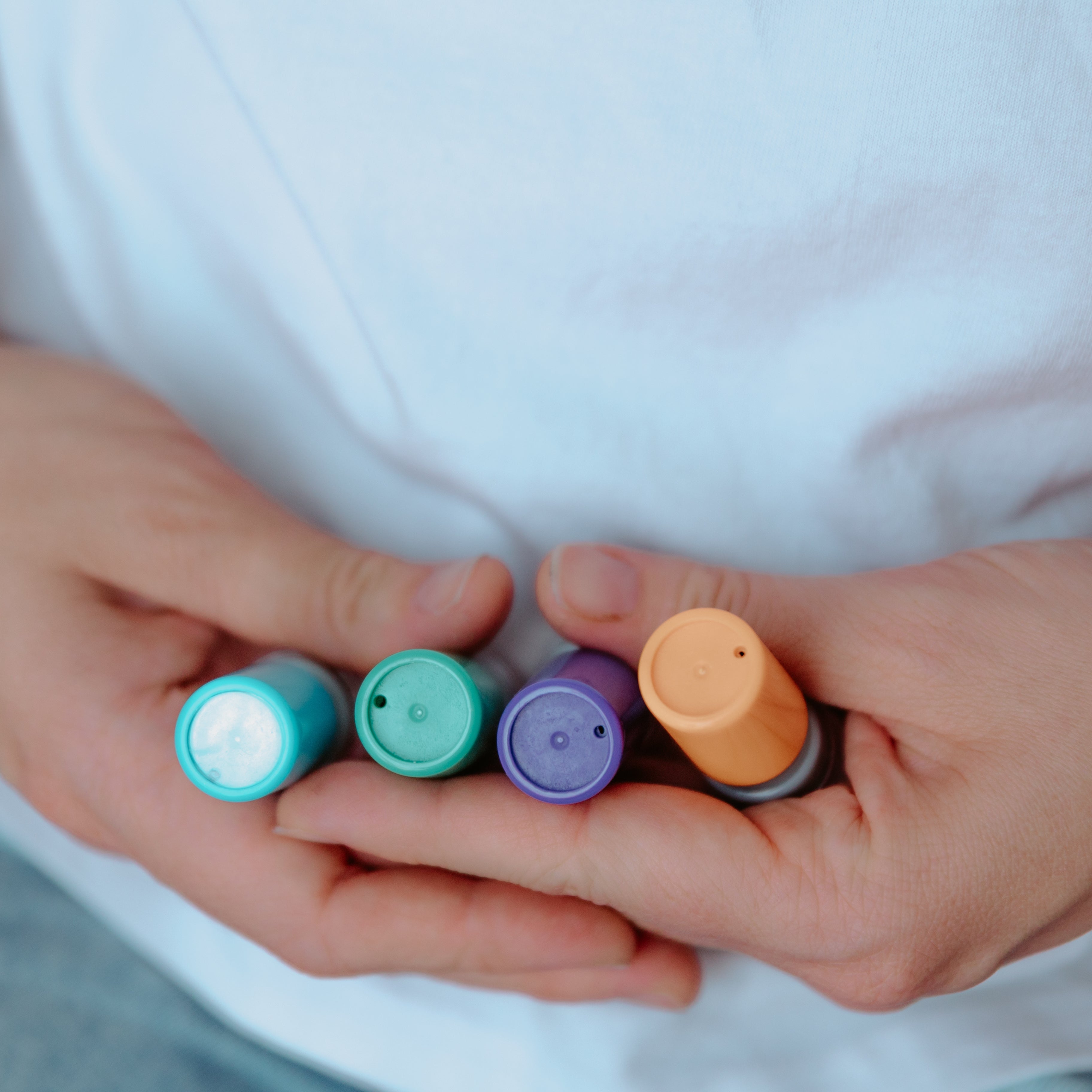 A person holding cylindrical card stamps side by side. A blue one, green one, purple one and yellow one