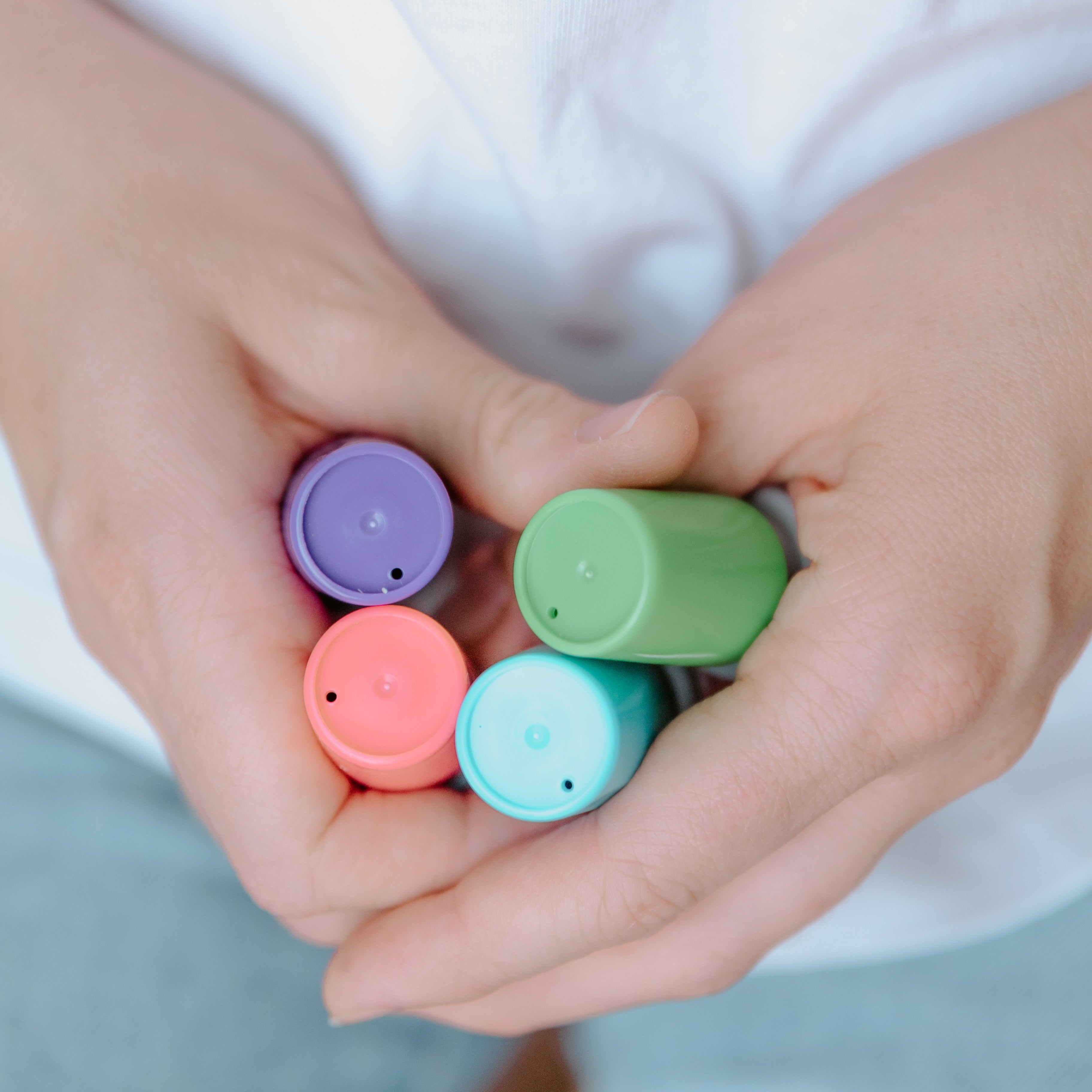 A person holding four cylindrical card stamps. A purple one, red one, white one and green one
