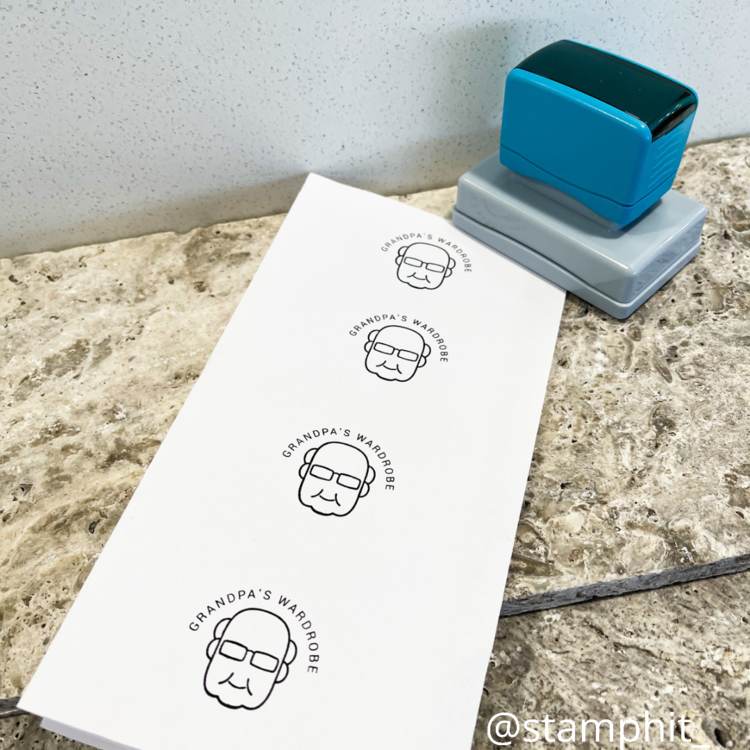 A blue business stamp with a grey, squared base sits next to a sheet of paper with a print of an old man that says 'Grandpa's wardrobe' in an arch