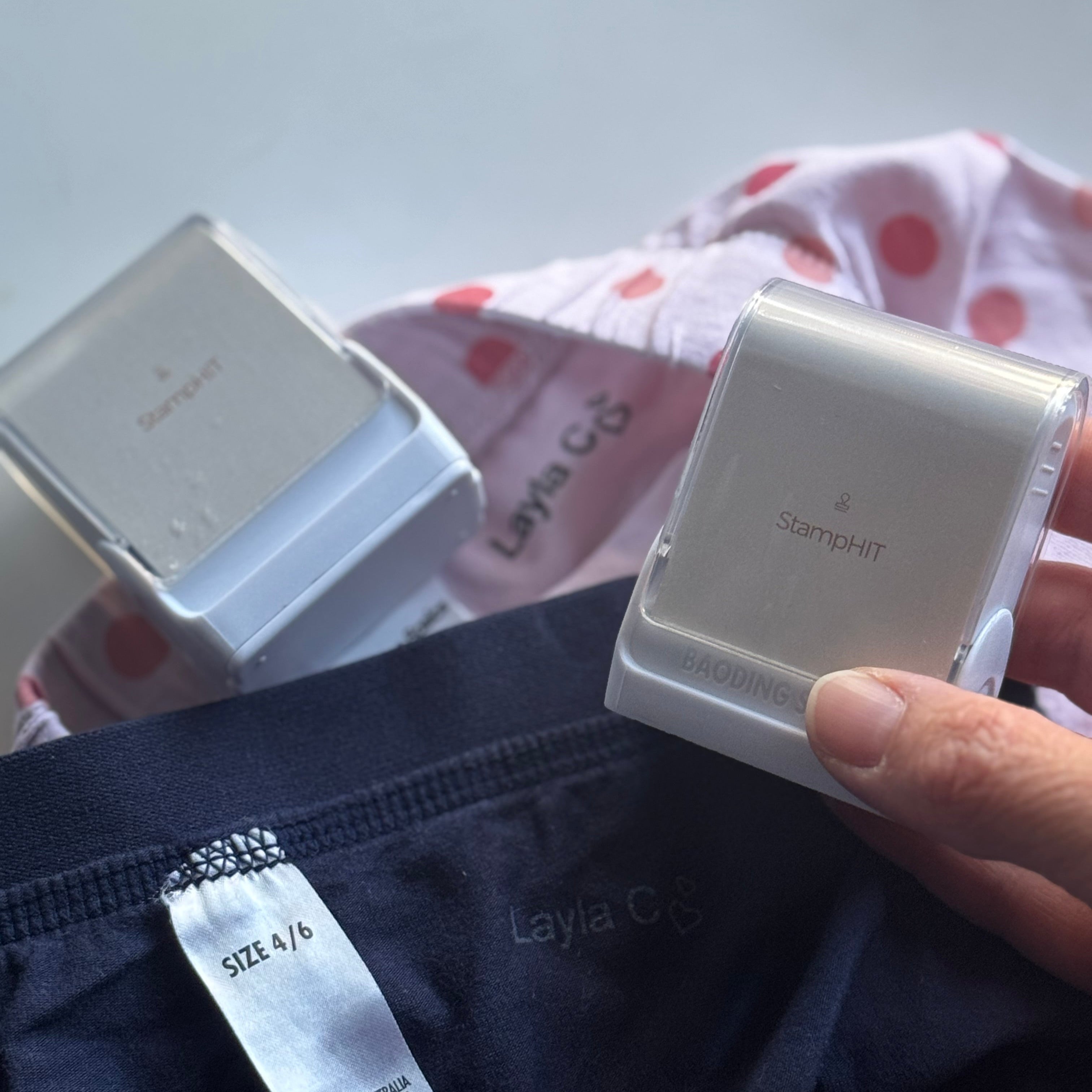 A hand holding one of a pair of StamHIT Fabric Name Stamps