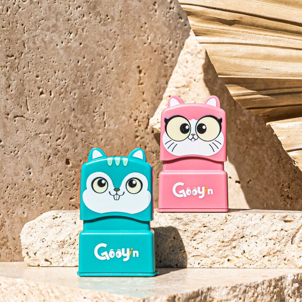 A cat stamp sitting behind a mouse stamp on an elevated surface both with 'Gooyin' printed on the front