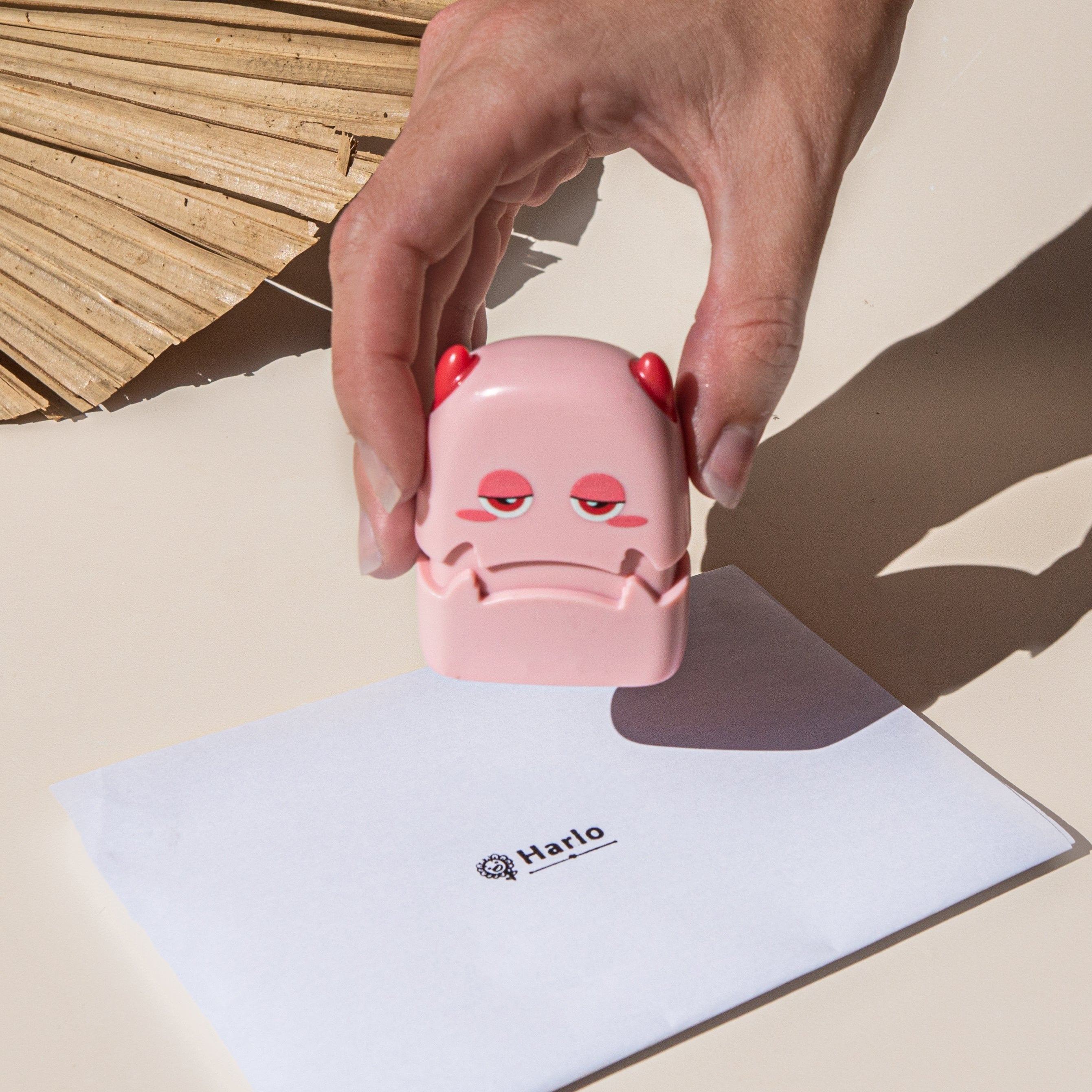 A person holding a pink monster fabric name stamp over a sheet of paper with 'Harlo' printed on it and a sunflower at the start