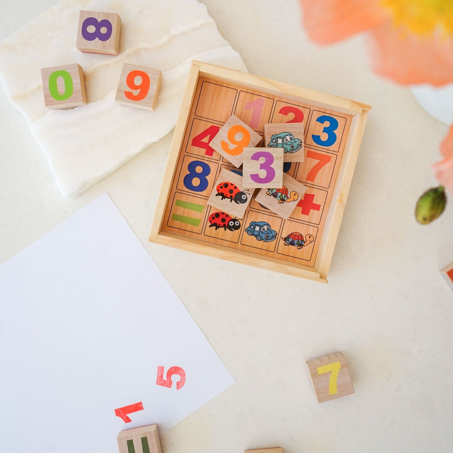 A wooden box with square education stamps with numbers, shapes and animals on them. With some blocks being outside the wooden box