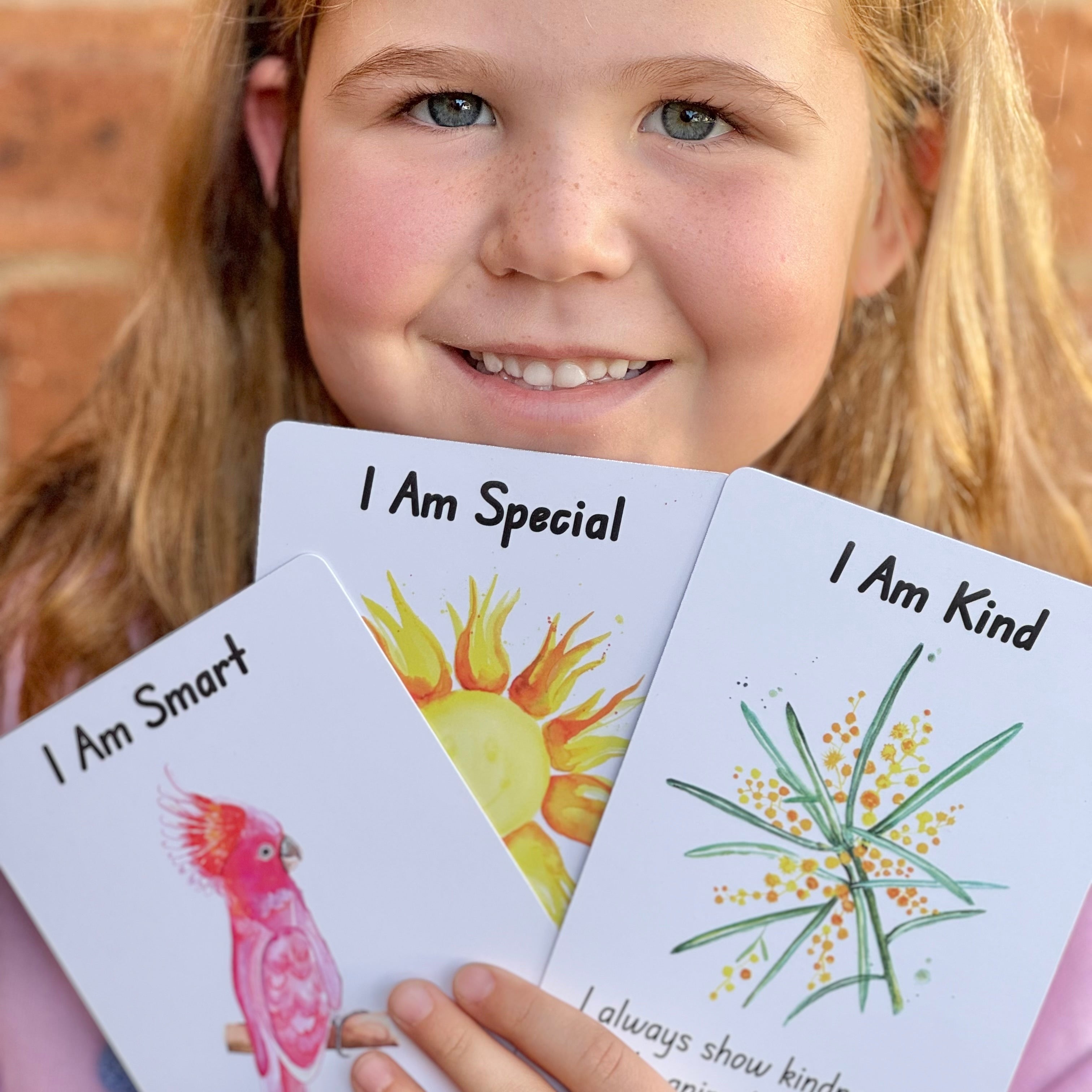 A young girl holds up three affirmation cards that say, I Am Smart, I am Special, I am Kind