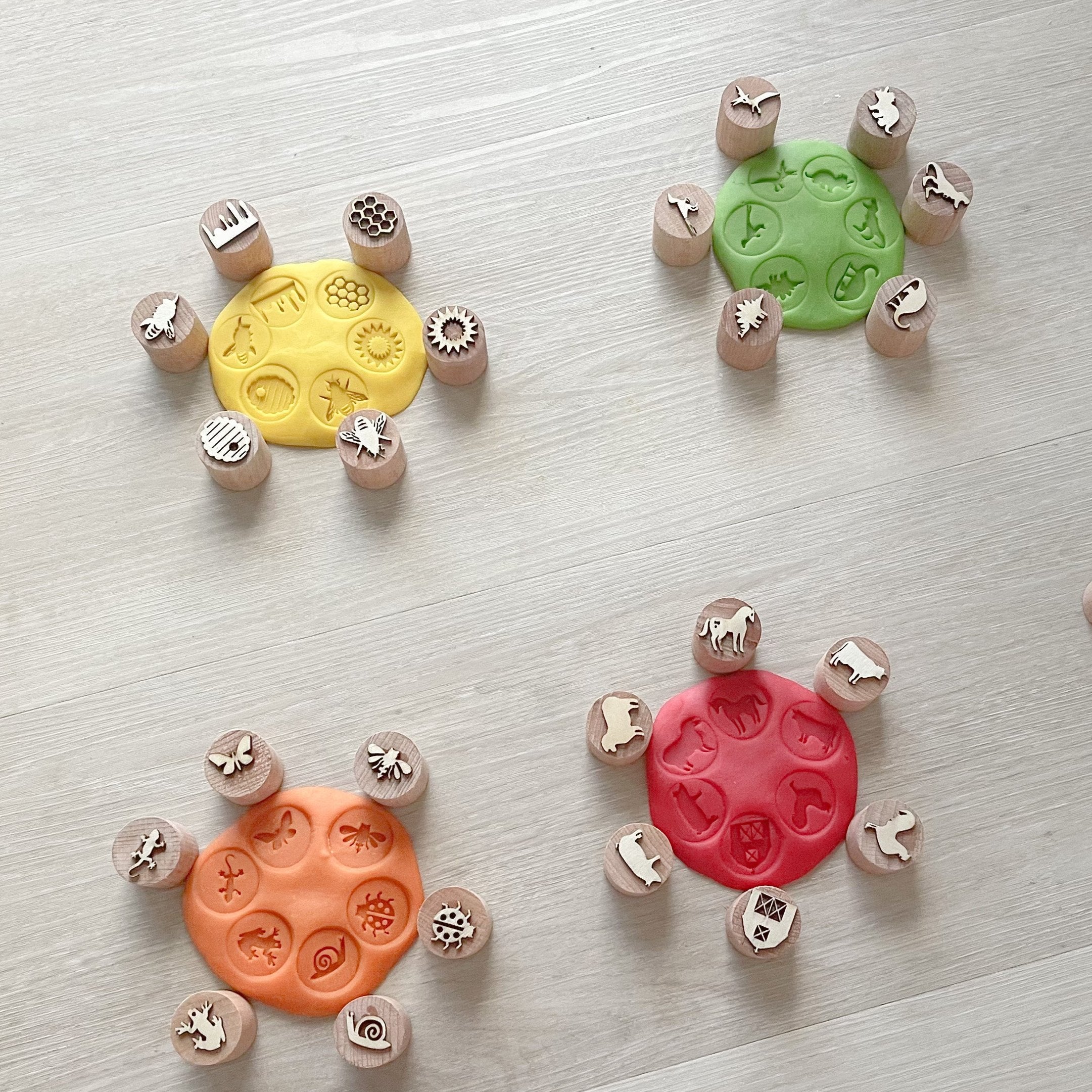 Multiple playdough stamps with various animal shapes around four sets of flat circular playdough rolls with shapes stamped into them