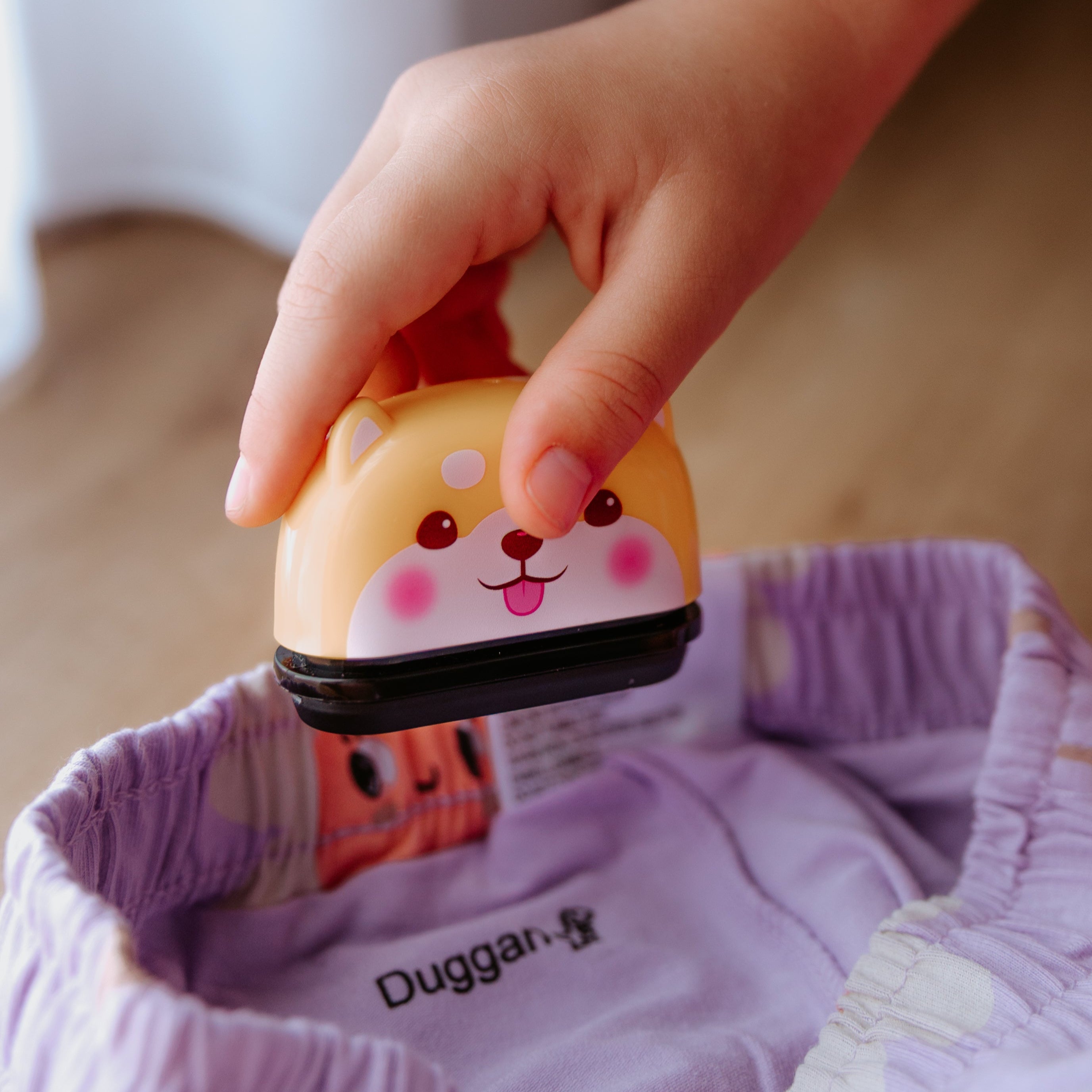 A person using an animal name stamp displaying a dog on a pink piece of clothing with the print displaying 'Duggan' with a dinosaur at the end