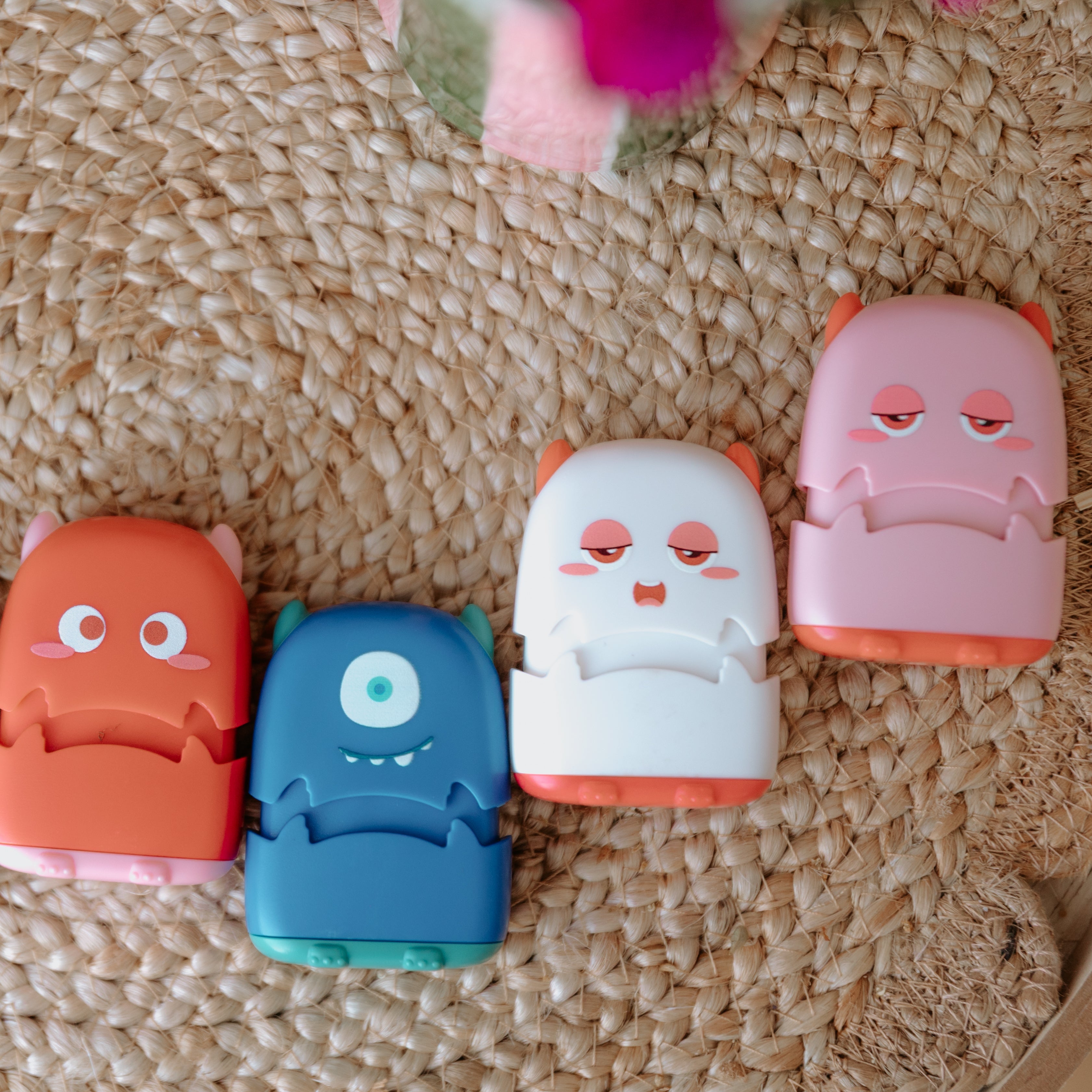Four monster fabric name stamps lay face up on a woven rug. A red one, blue one, white one and pink one