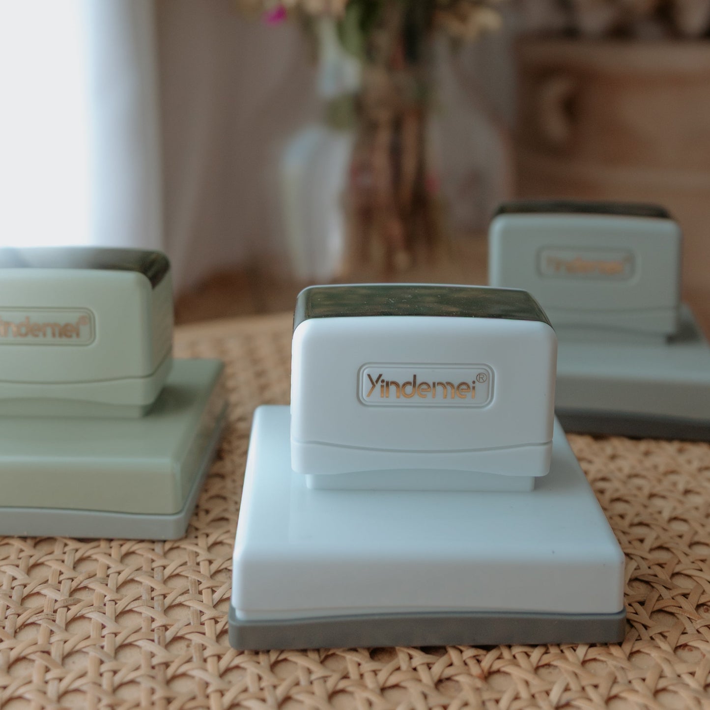 Three white business stamps with squared bases on a table facing the camera with text that displays 'Yindemei'