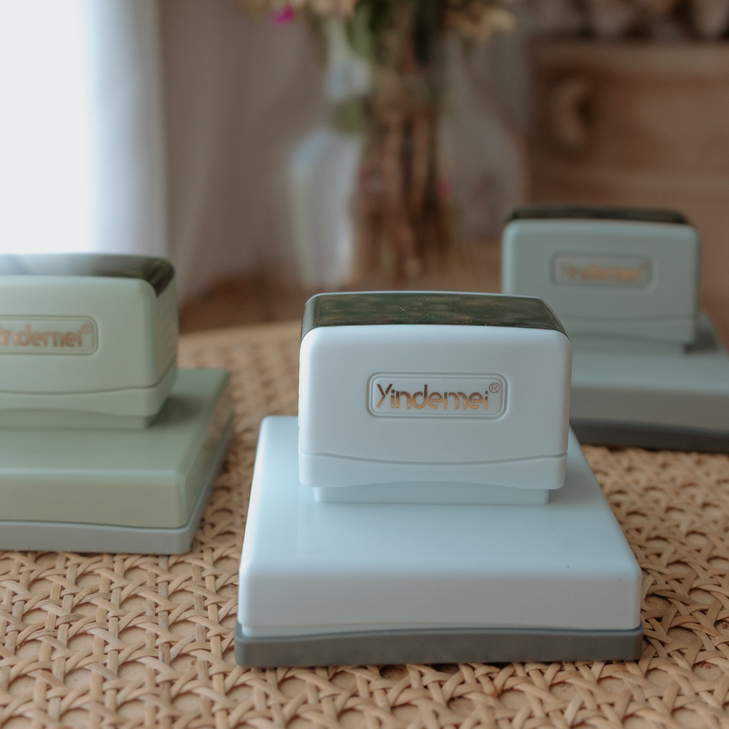 Three white business stamps with squared bases on a table facing the camera with text that displays 'Yindemei'