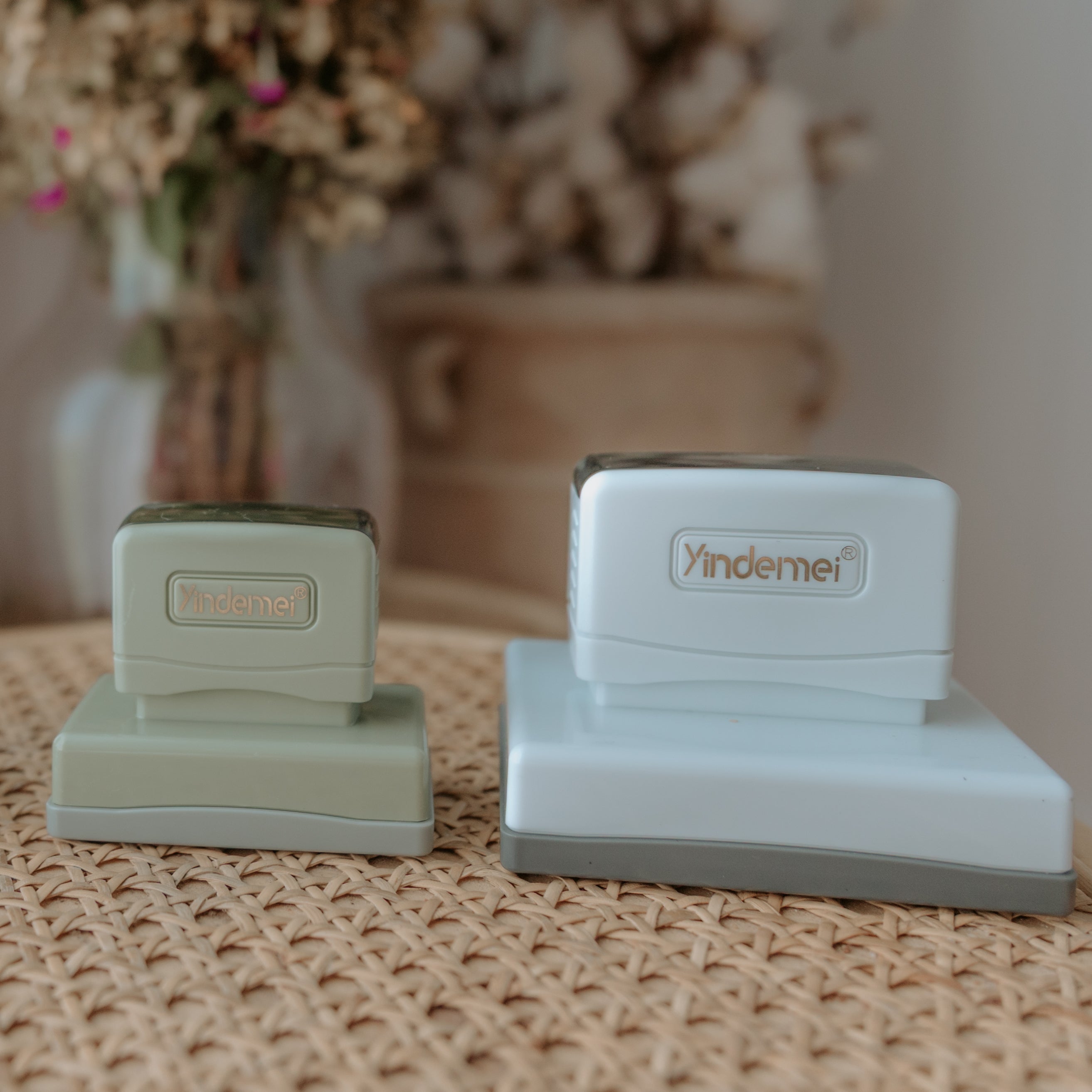 A small, green business stamp sitting next to a large, white business stamp both with squared bases and displaying 'Yindemei' text on the handle