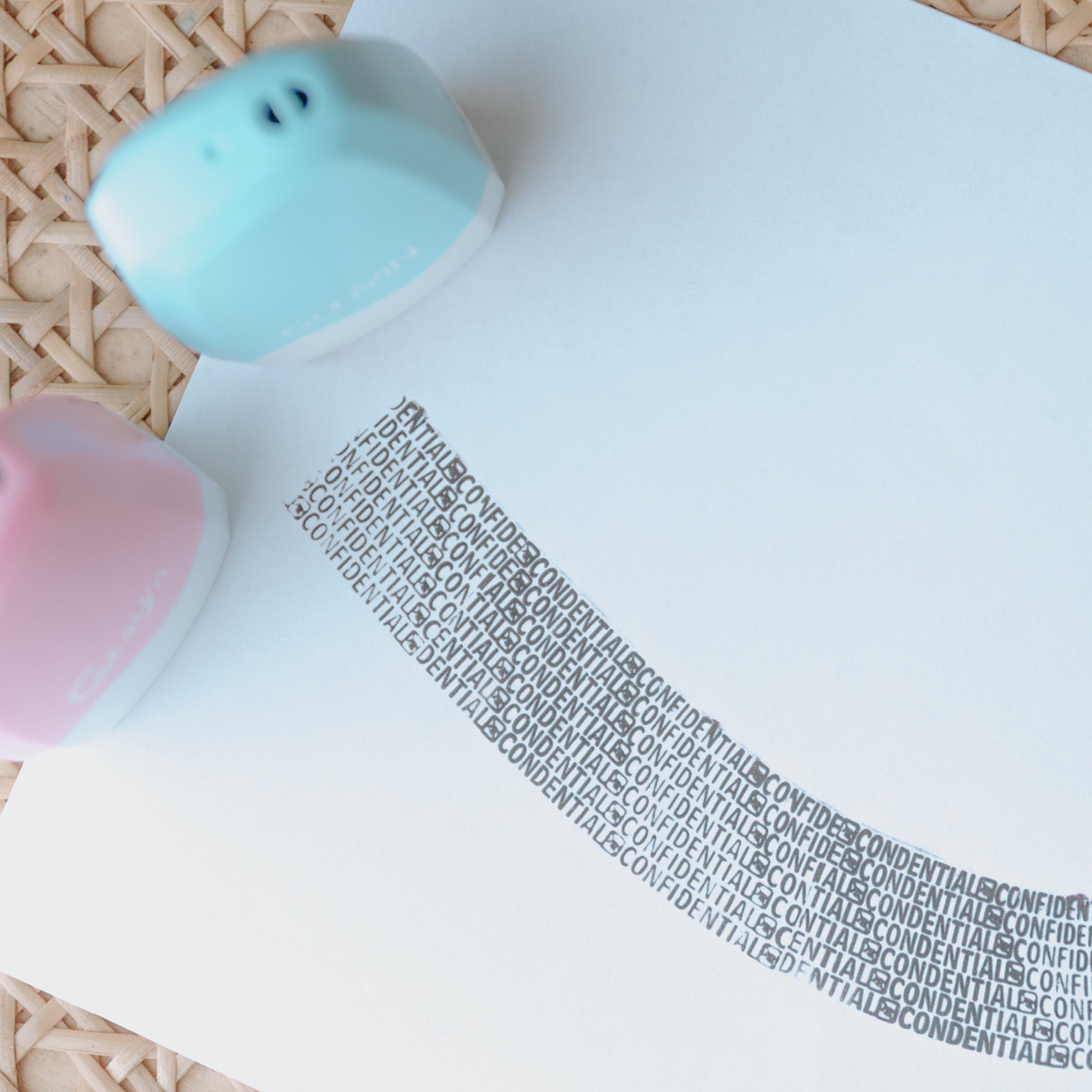 Two privacy stamps, one light blue one pink, standing upright on a sheet of paper with ink that prints 'confidential' across it