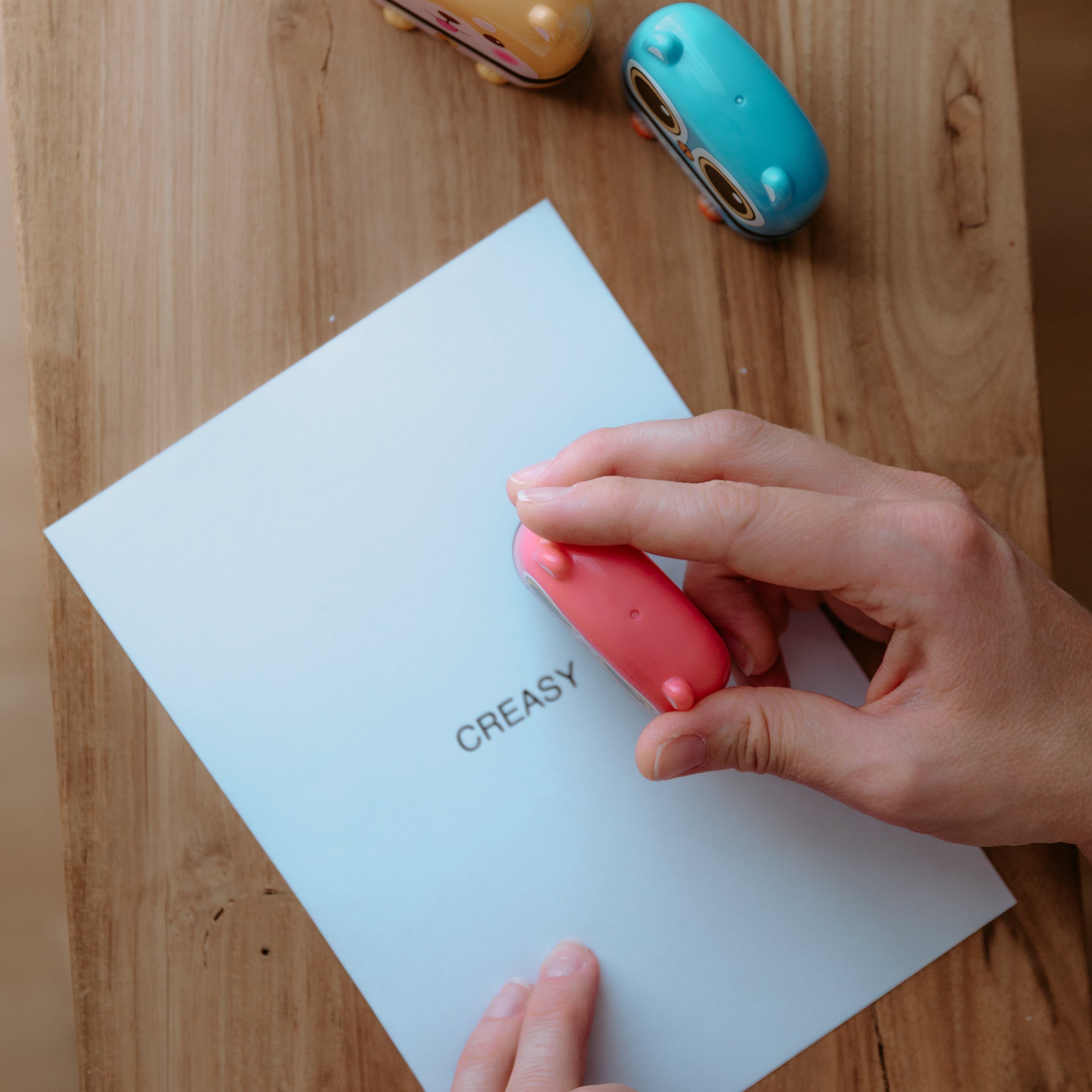 A top-down angle of a person using an animal name stamp displaying a cat on a sheet of paper with an already printed text displaying 'CREASY' with two other animal name stamps sitting on the table off to the side