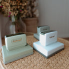 White, green and grey business stamps with squared bases sitting on a table with 'Yindemei' text displayed on them
