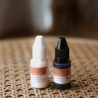 Black and white fabric ink refill bottles sitting upright next to each other with the stampHIT logo on the front of both