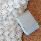 A white rectangular clothing name stamp with a curved top, leaning on a woven cloth displaying the StampHIT logo 