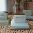 Three white business stamps with squared bases on a table facing the camera with text that displays 'Yindemei' 